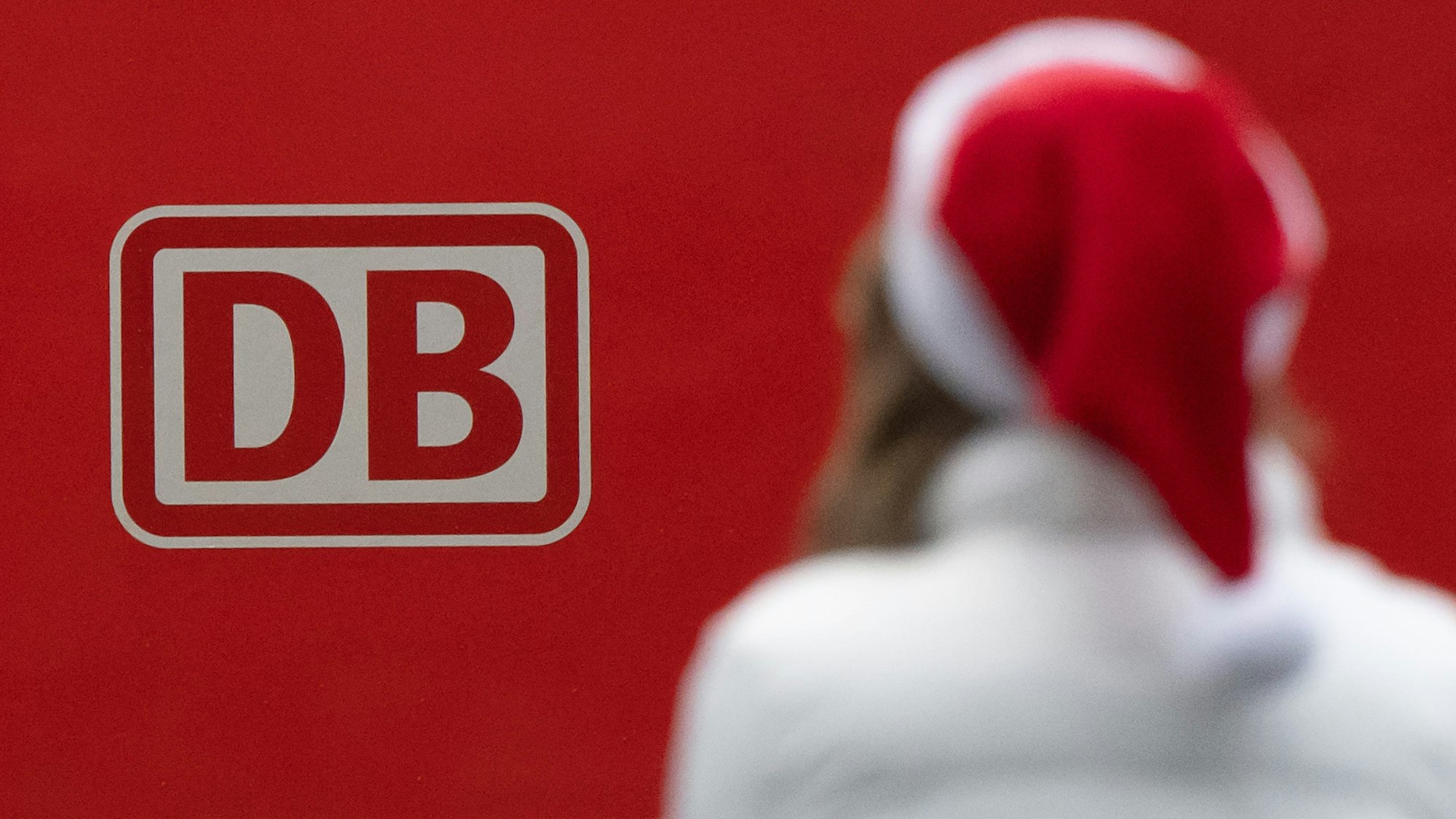 Eine Frau steht am Hauptbahnhof in Frankfurt/Main mit Weihnachtmütze vor einem Logo der Deutschen Bahn (Archivbild 2022): Ein Weihnachtsgruß des Unternehmens geht auf Instagram nach hinten los.