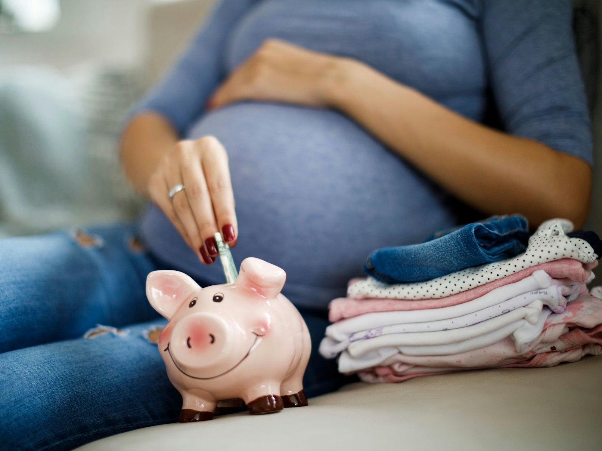 Eine schwangere Frau steckt Geld in ein Sparschwein.