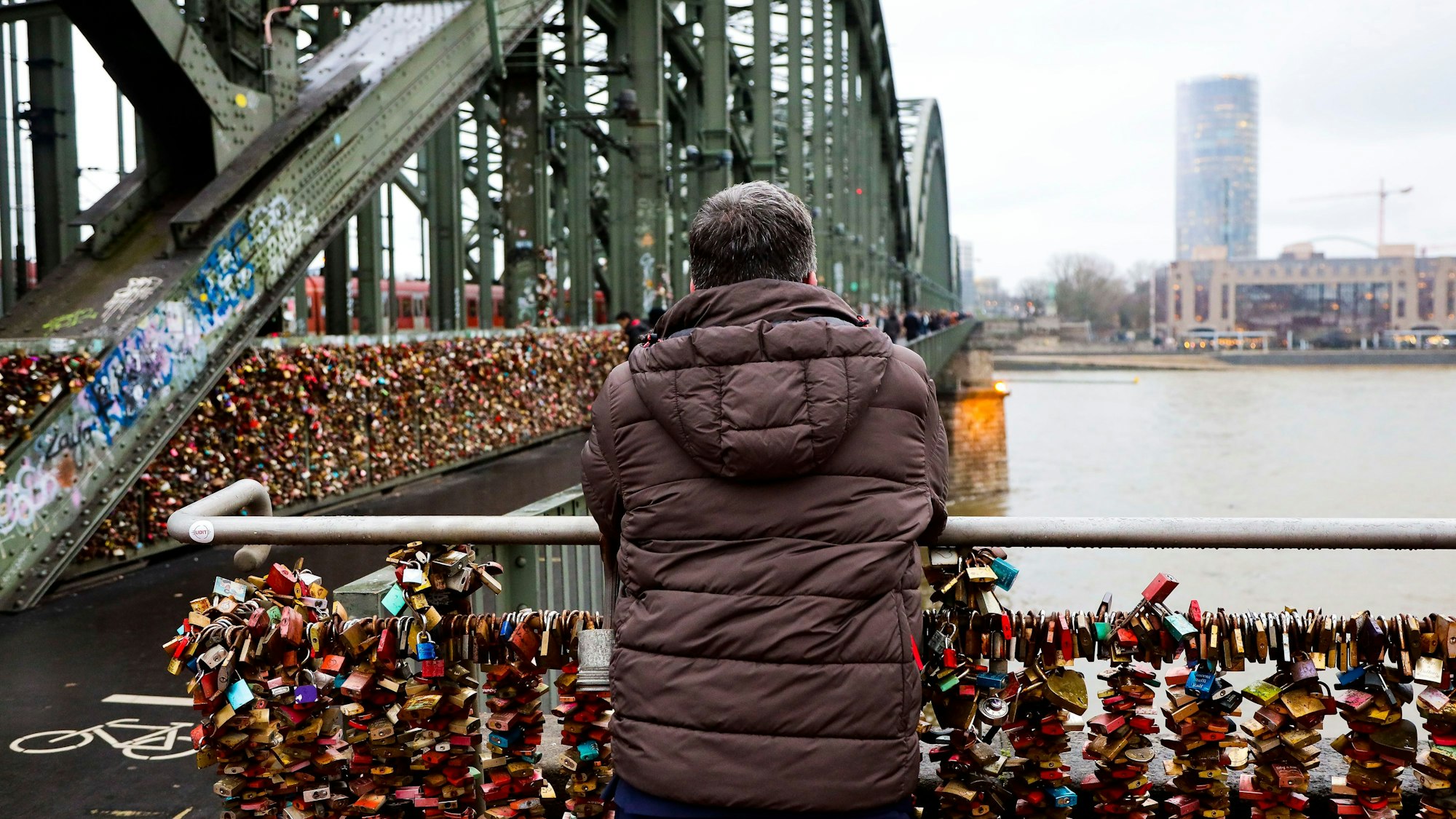 Ein Mann steht auf der Hohenzollernbrücke und blickt auf den Rhein