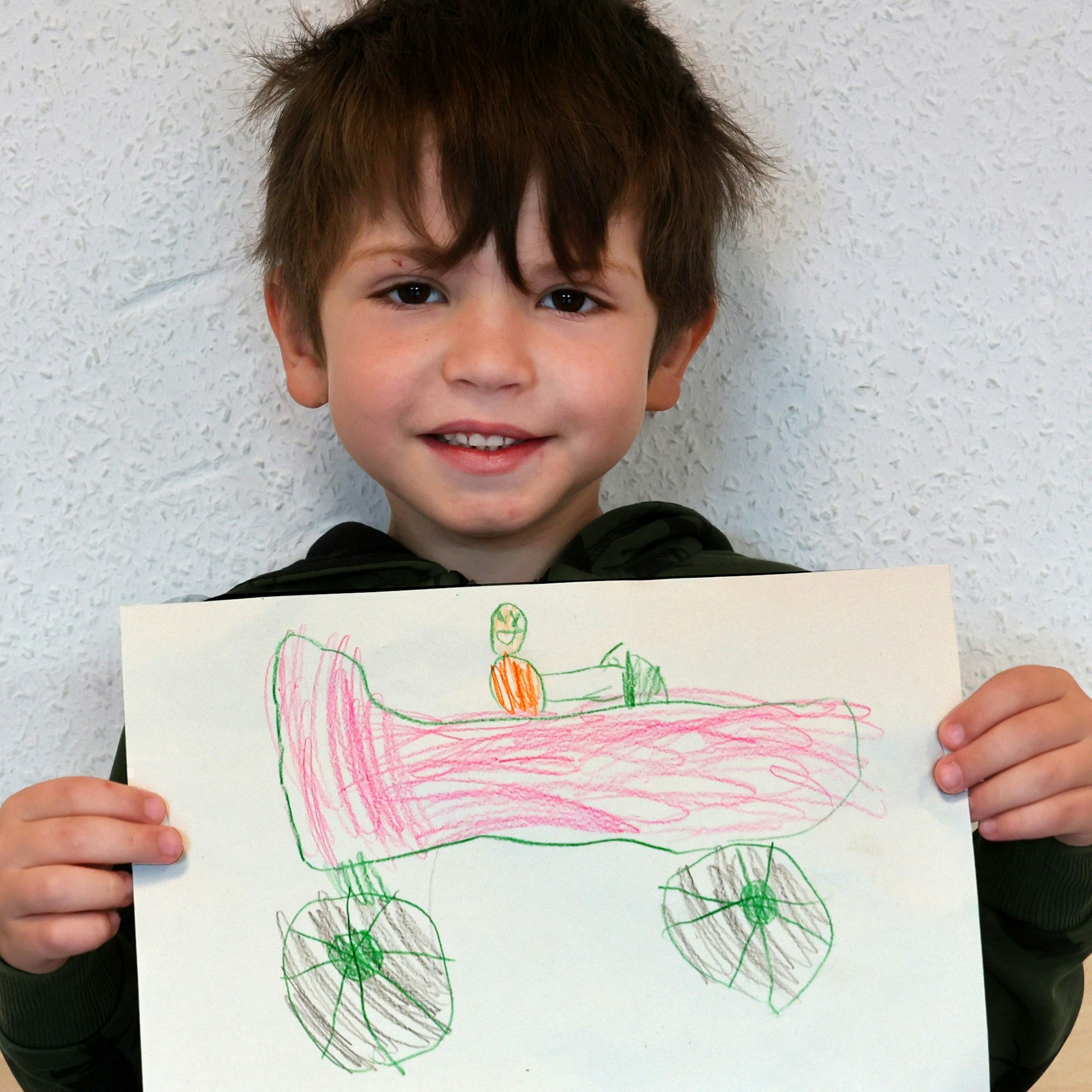 Ein Junge hält einen gemalten Wunschzettel in der Hand und blickt in die Kamera.

