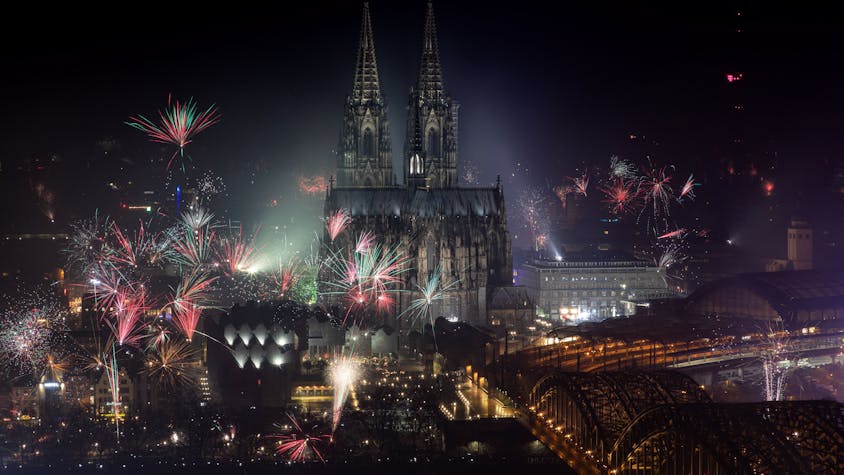 Feuerwerk explodiert zum Jahreswechsel rund um den Kölner Dom, dieser und die Hohenzollernbrücke ist angeleuchtet.