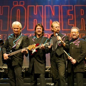 Peter Werner, Hannes Schöner, Pete Bauchwitz, Henning Krautmacher, Janus Fröhlich und Ralf Rudnik stehen im schwarzen Anzug auf einer Bühne.