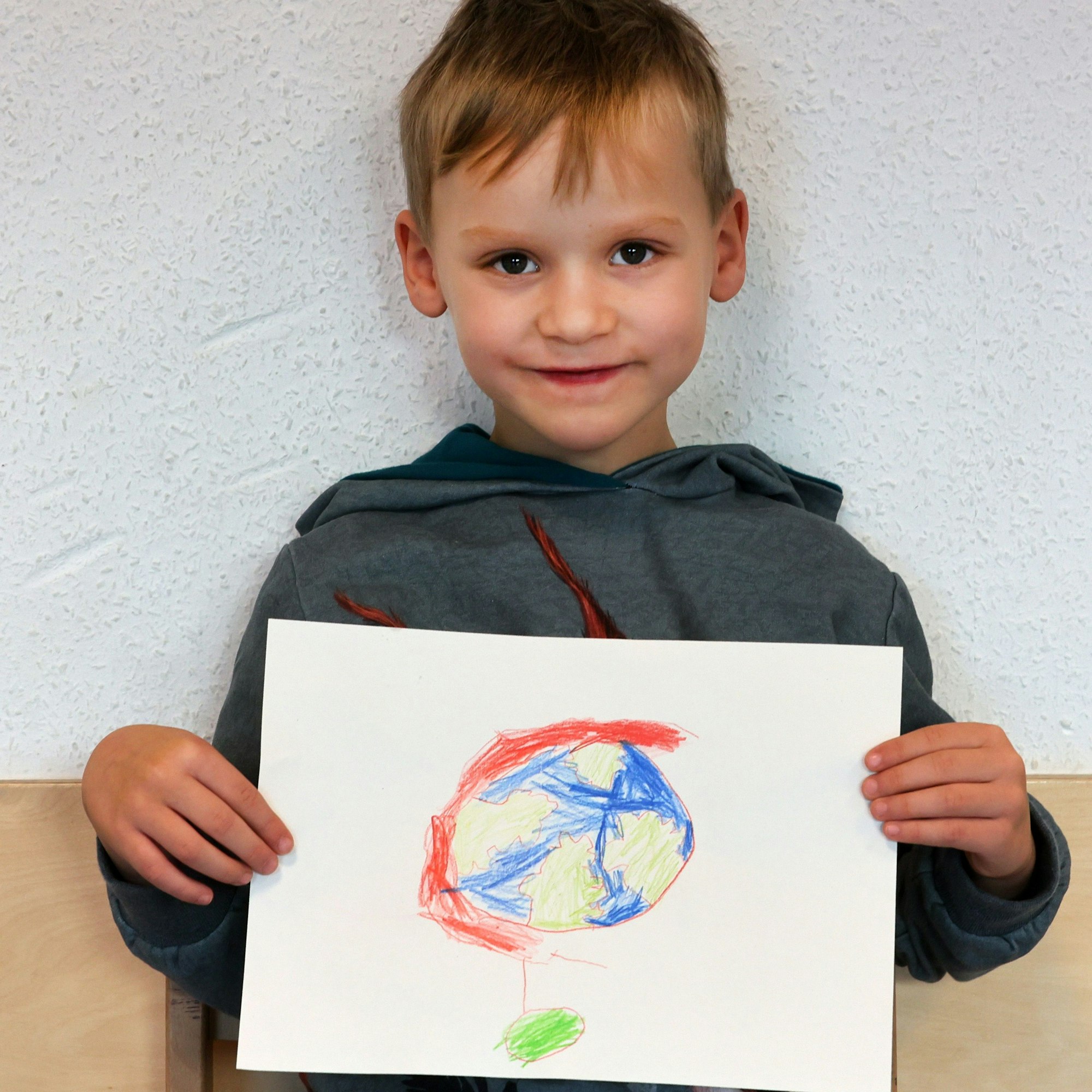 Ein Junge hält einen gemalten Wunschzettel in der Hand und blickt in die Kamera.

