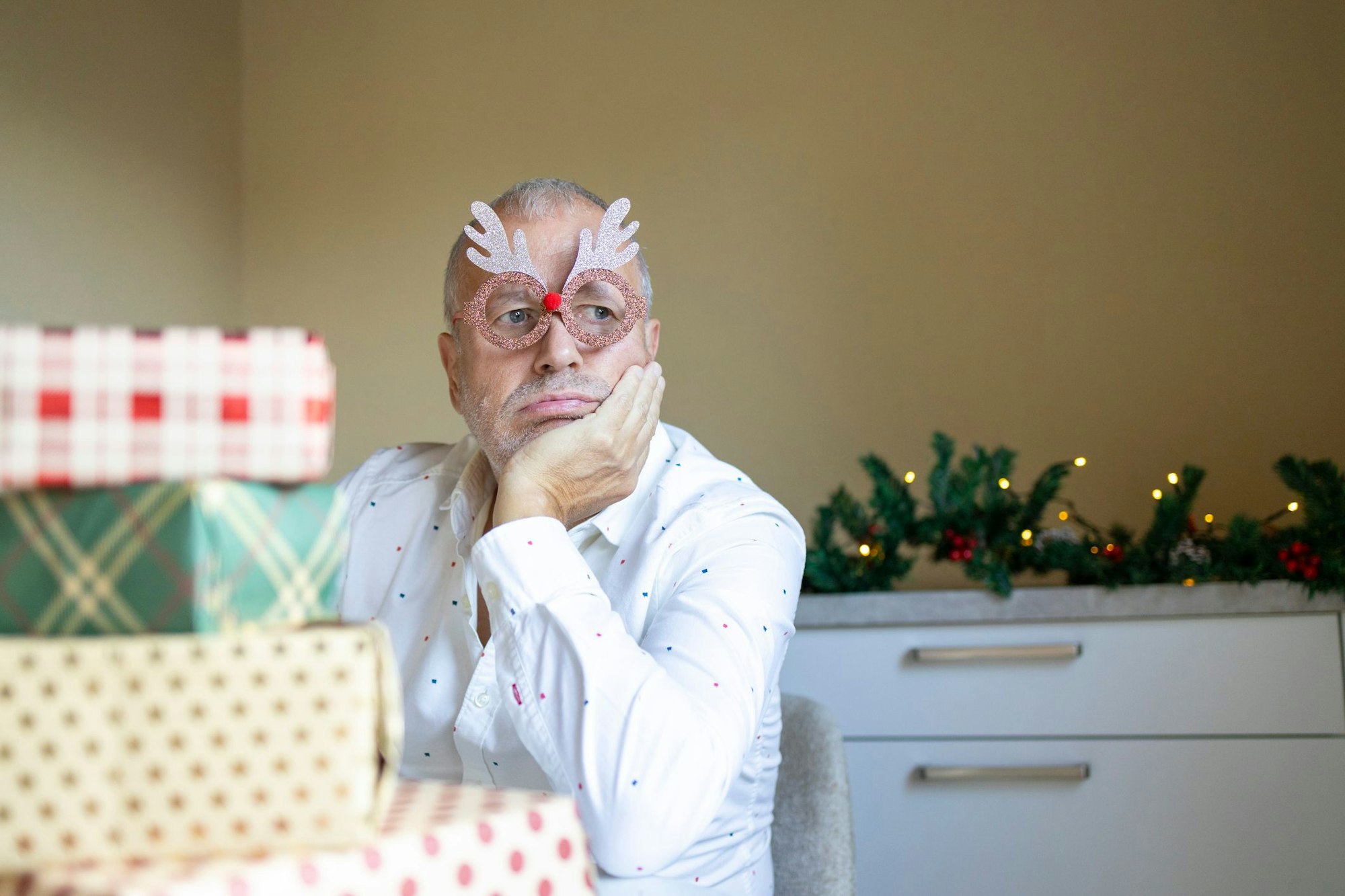 Upset aged man with grey hairs sitting near Christmas presents