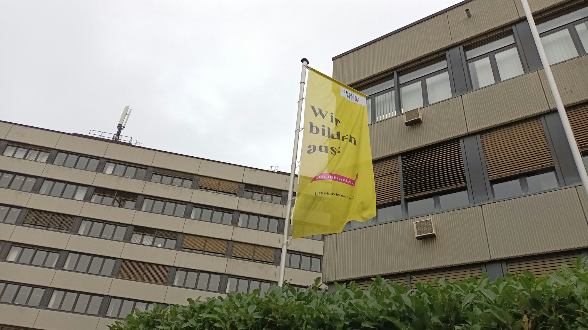 Das Bild zeigt die Fassade des Amtsgerichts in Siegburg mit einer Hecke und einer gelben Flagge.