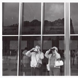 Menschen fotografieren den Mount Rushmore durch eine Glasscheibe hindurch.&nbsp;