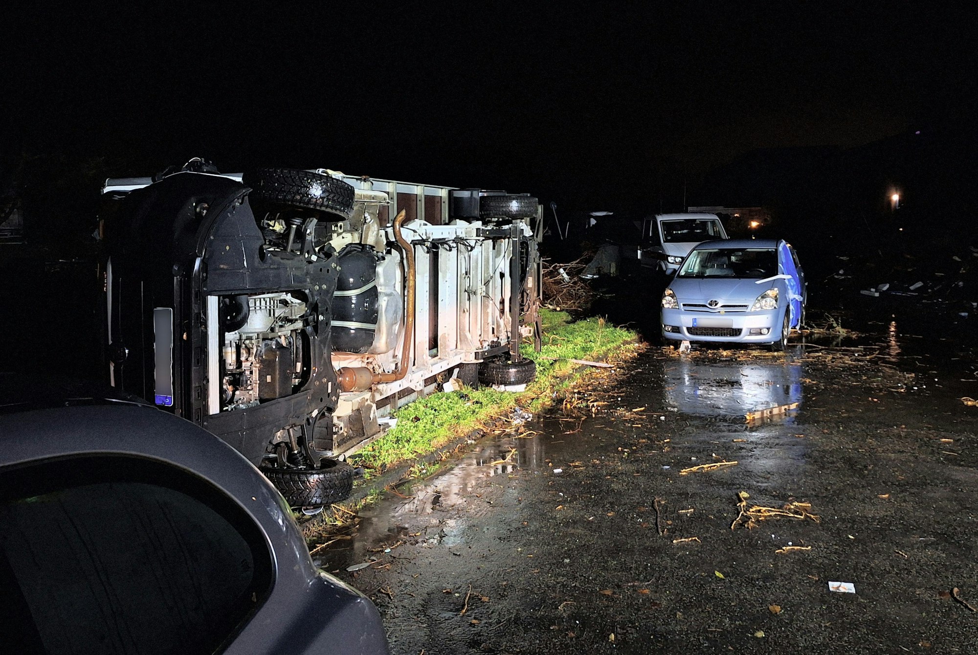 Beschädigte Autos und ein umgekippter Laster liegen neben abgebrochenen Ästen in Köln.