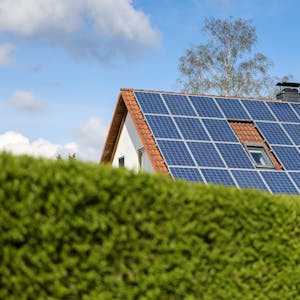 Haus mit Photovoltaik auf dem Dach hinter einer grünen Hecke.