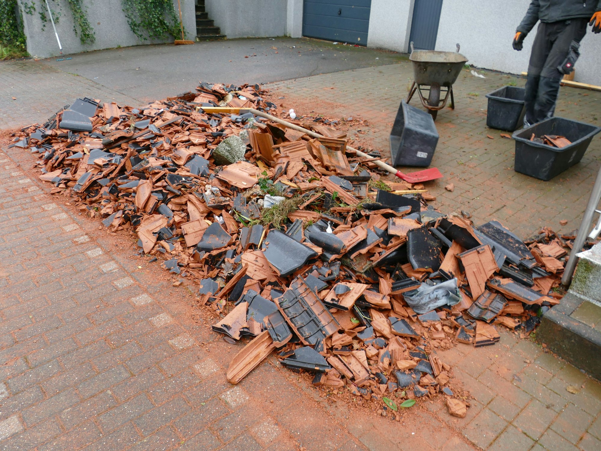 Ein Haufen Schutt aus Dachschindeln und Ästen liegt zusammengekehrt in der Einfahrt eines Wohnhauses.