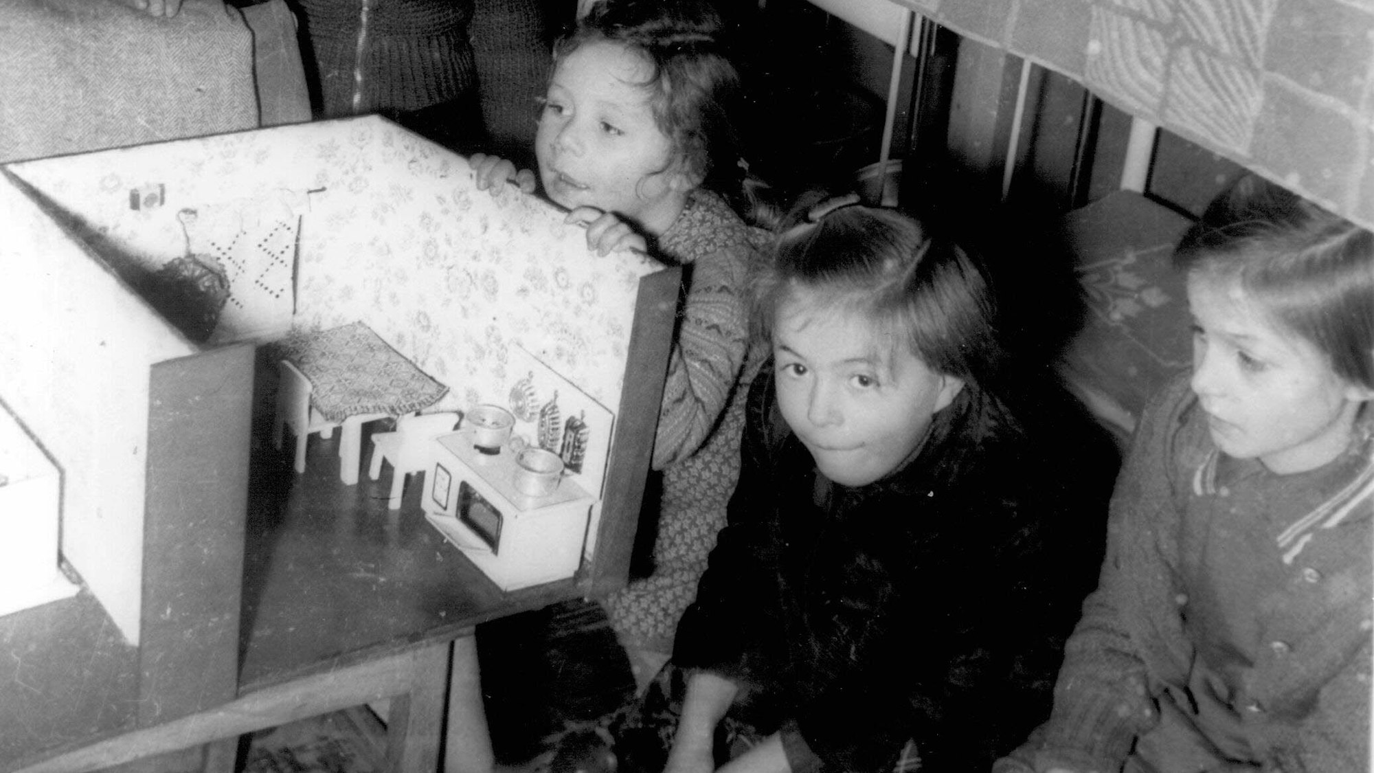 Vier kleine Mädchen freuen sich Weihnachten 1955 über ein Puppenhaus.