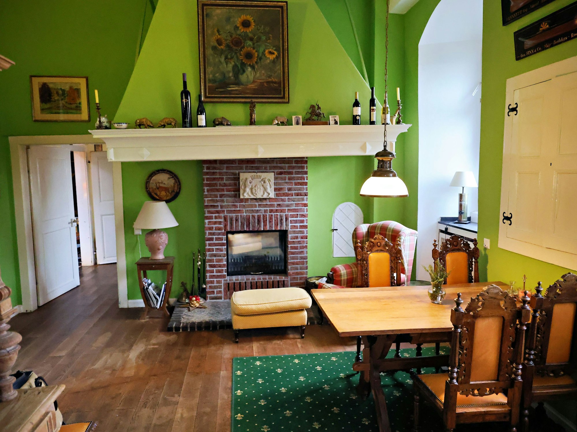 Das Zimmer mit dem gemauerten offenen Kamin ist grün tapeziert.