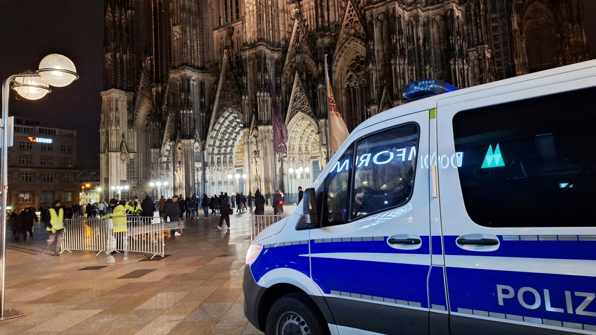 Ein Einsatzfahrzeug der Polizei steht vor dem Dom. Einen Tag vor Weihnachten erhöht die Polizei in Köln wegen möglichen Anschlagsplänen ihre Schutzmaßnahmen.