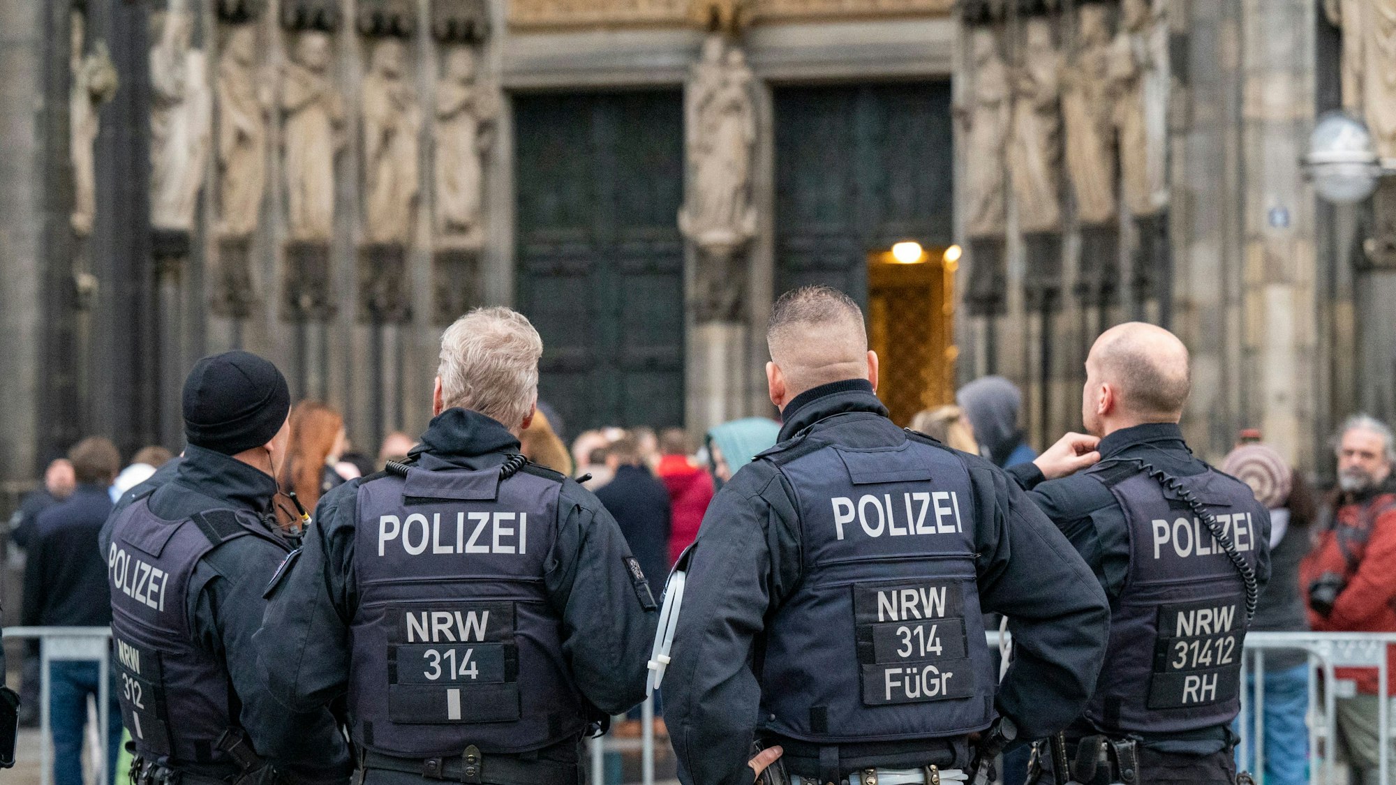 Köln: Wegen eines befürchteten Anschlags kontrolliert die Polizei alle Besucher des Doms. Zu sehen sind die Hinteransichten von vier Polizisten vor dem Hauptportal des Doms.