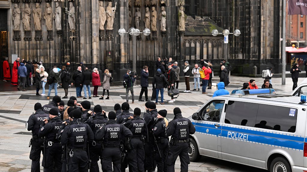Einige Einsatzkräfte der Polizei stehen ganz in schwarz gekleidet vor dem Haupteingang des Kölner Doms.