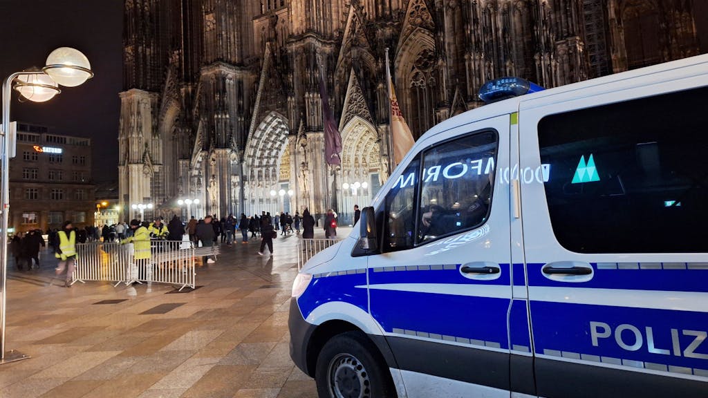 Ein Polizei-Auto steht auf der Freifläche vor dem Kölner Dom, im Hintergrund sind viele Menschen zu sehen.