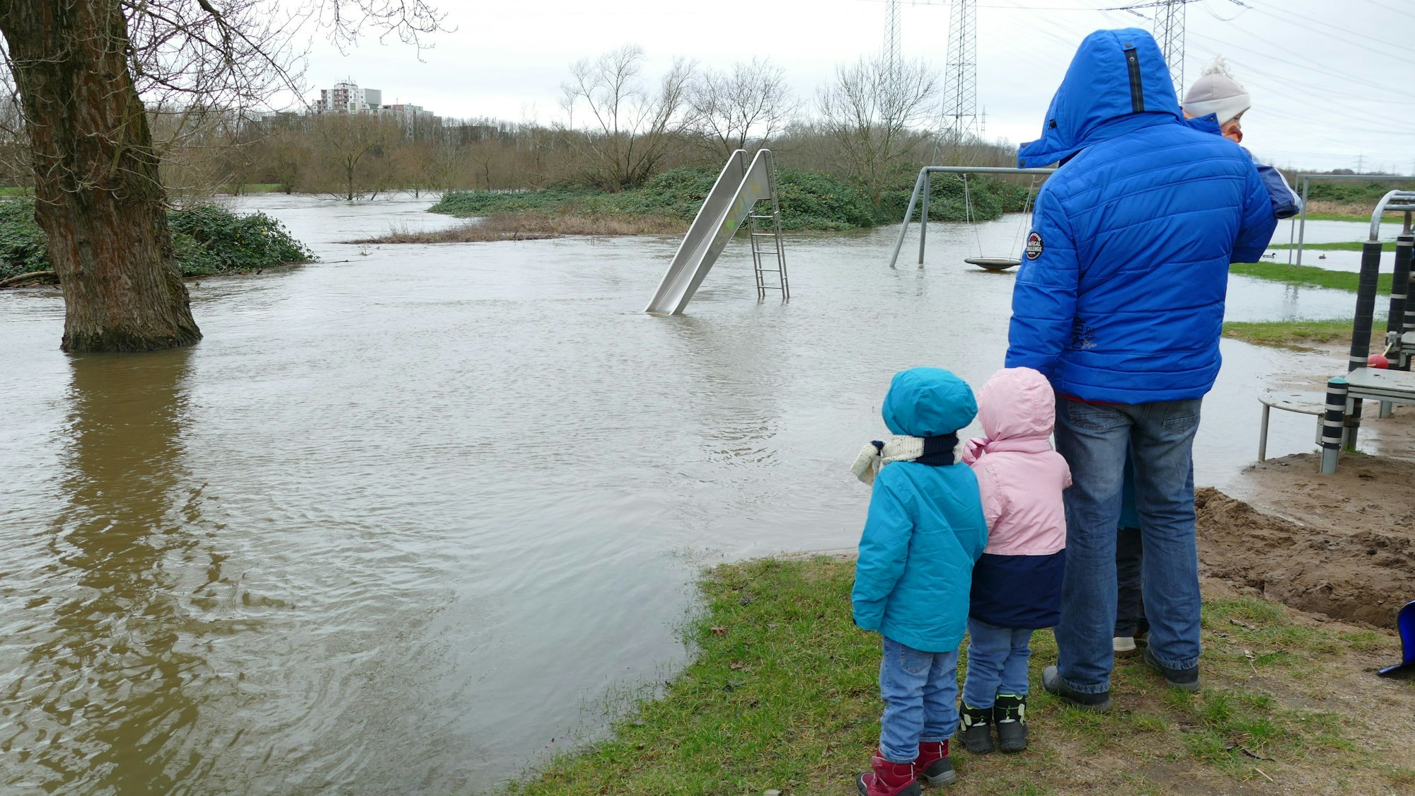 Der Spielplatz an der Sieg in Siegburg-Zange ist überflutet. Dort stehen Kinder und blicken mit ihrem Vater aufs Wasser.
