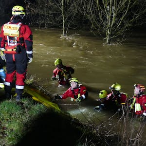 Angehörige des DLRG in Tauchanzügen und Helmen mit Kopflampen stehen bis zur Brust im reißenden Fluss.