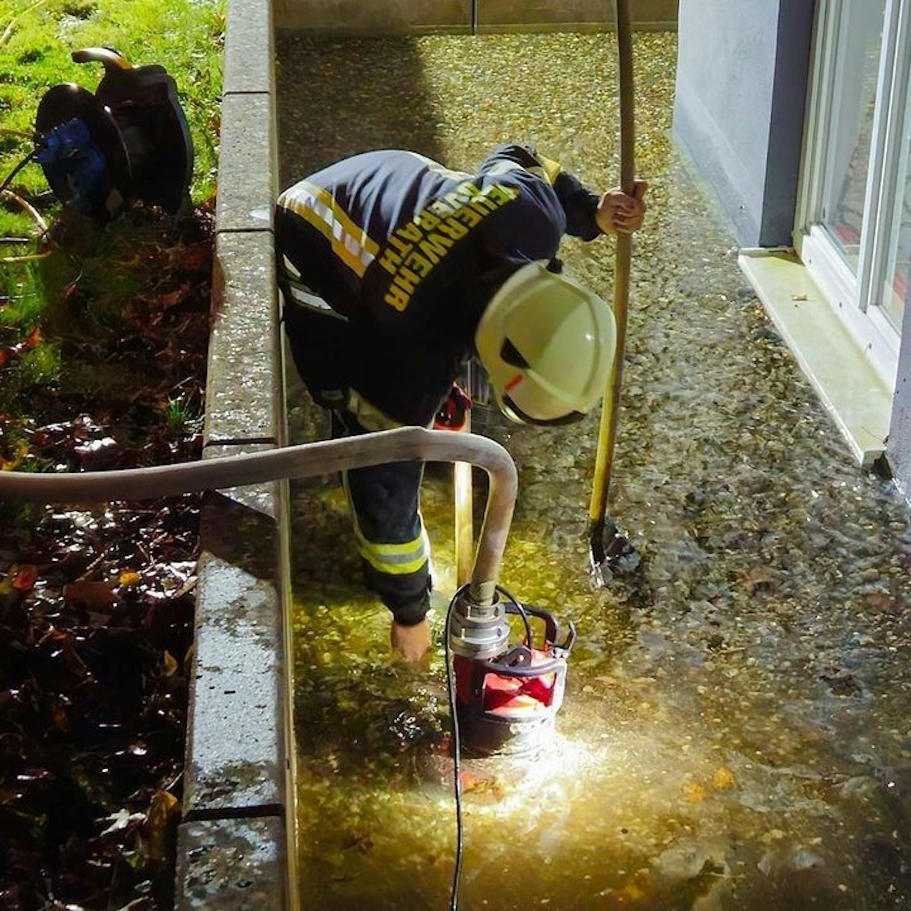 Ein Feuerwehrmann pumpt vor einem Fenster Wasser mit einer Tauchpumpte ab.