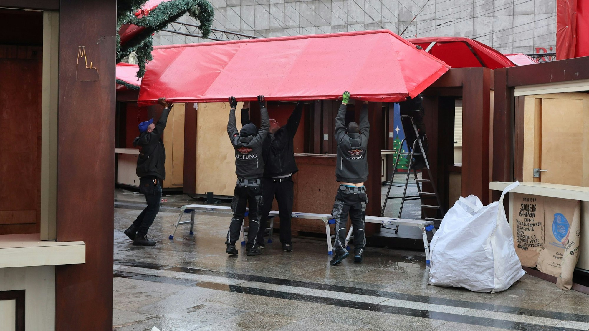 Mehrere Männer arbeite zusammen, um eine Hütte des Weihnachtsmarkts am Kölner Dom zu demontieren.

