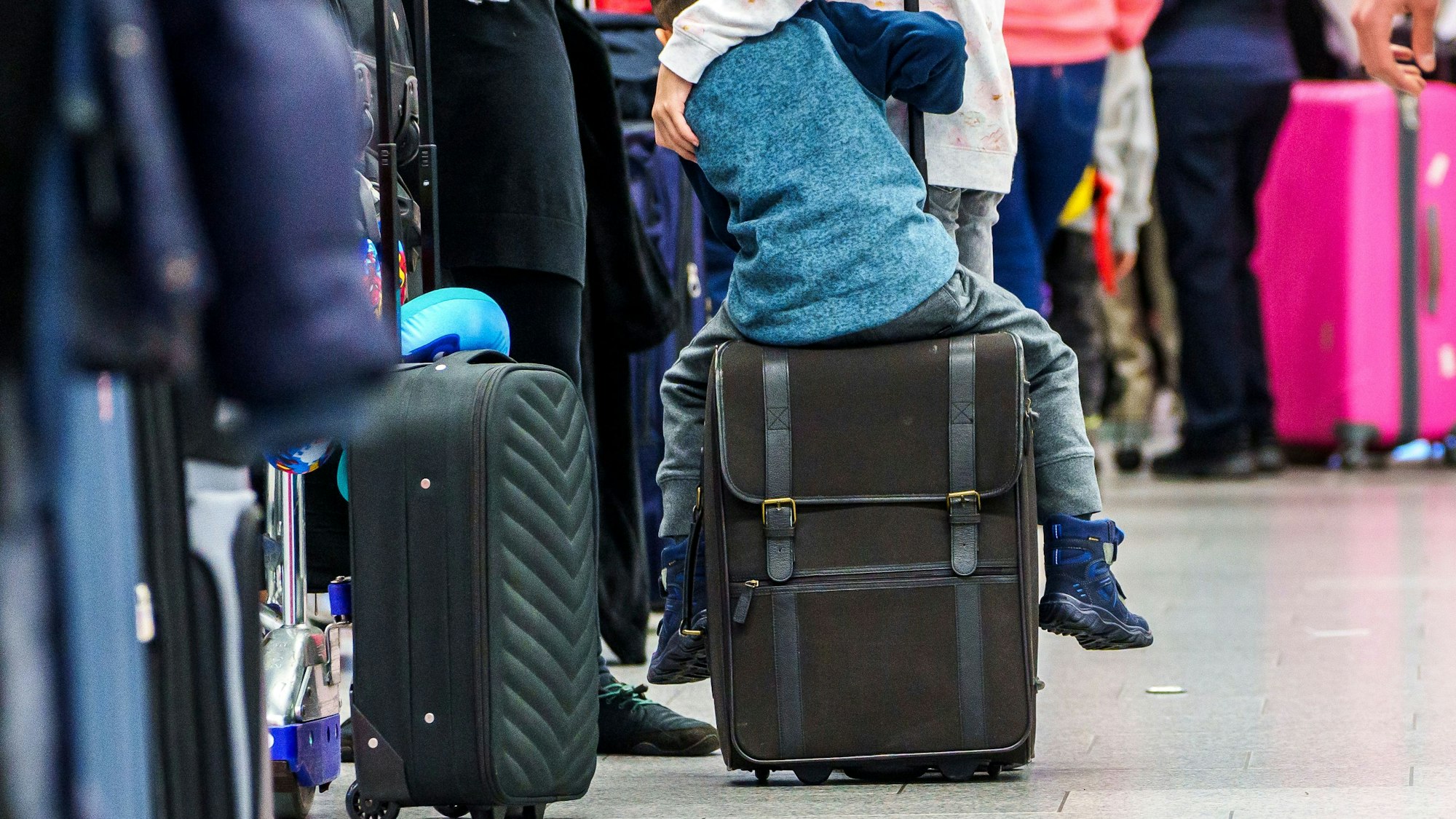 Ein Kind sitzt in der Warteschlange auf seinem Koffer.