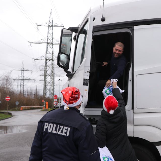 Polizisten reichen einem Fernfahrer eine Tüte in seinen Lkw.