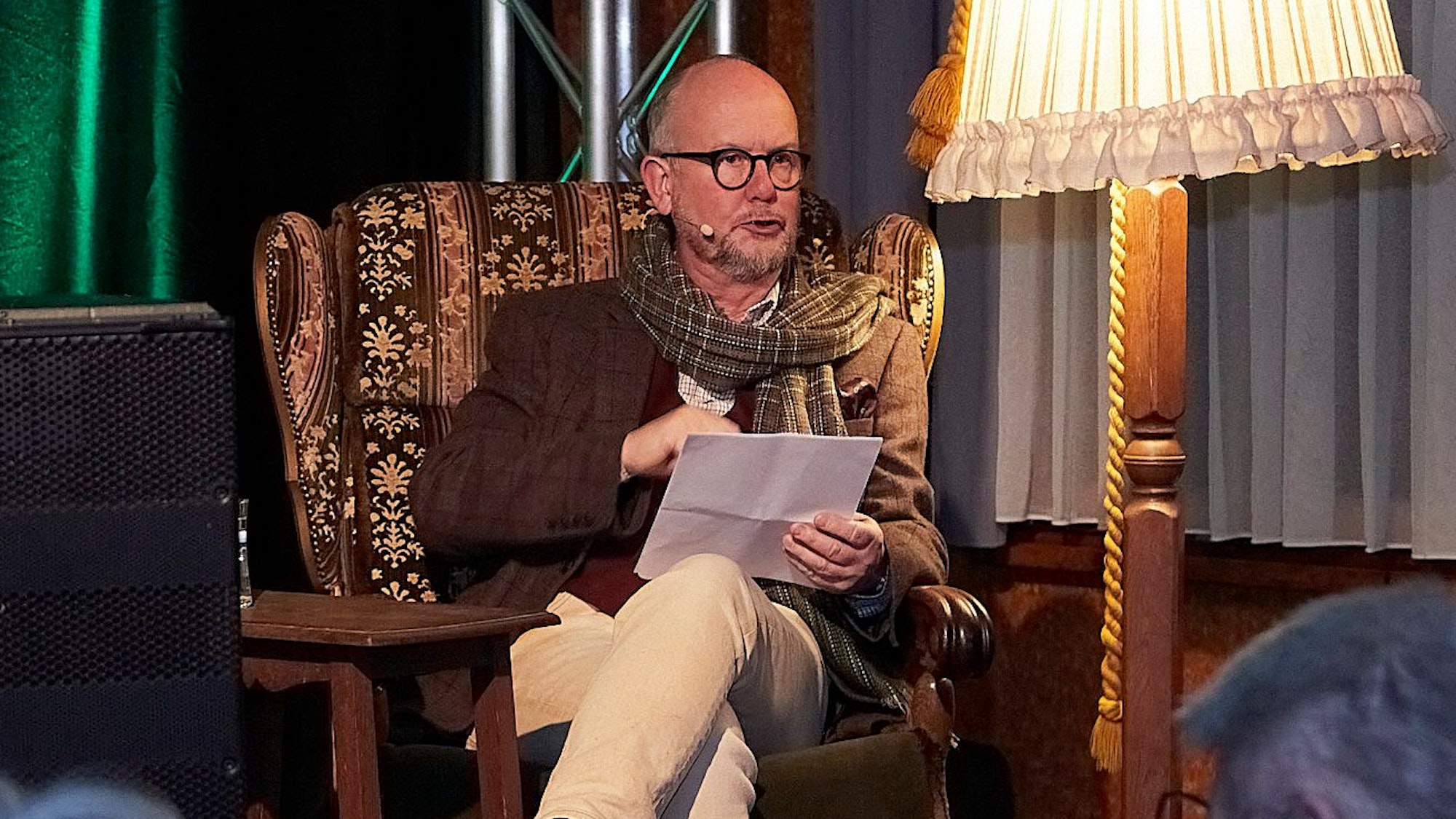 Ralf Kramp sitzt in einem Sessel und liest vor, neben ihm eine alte Stehlampe.