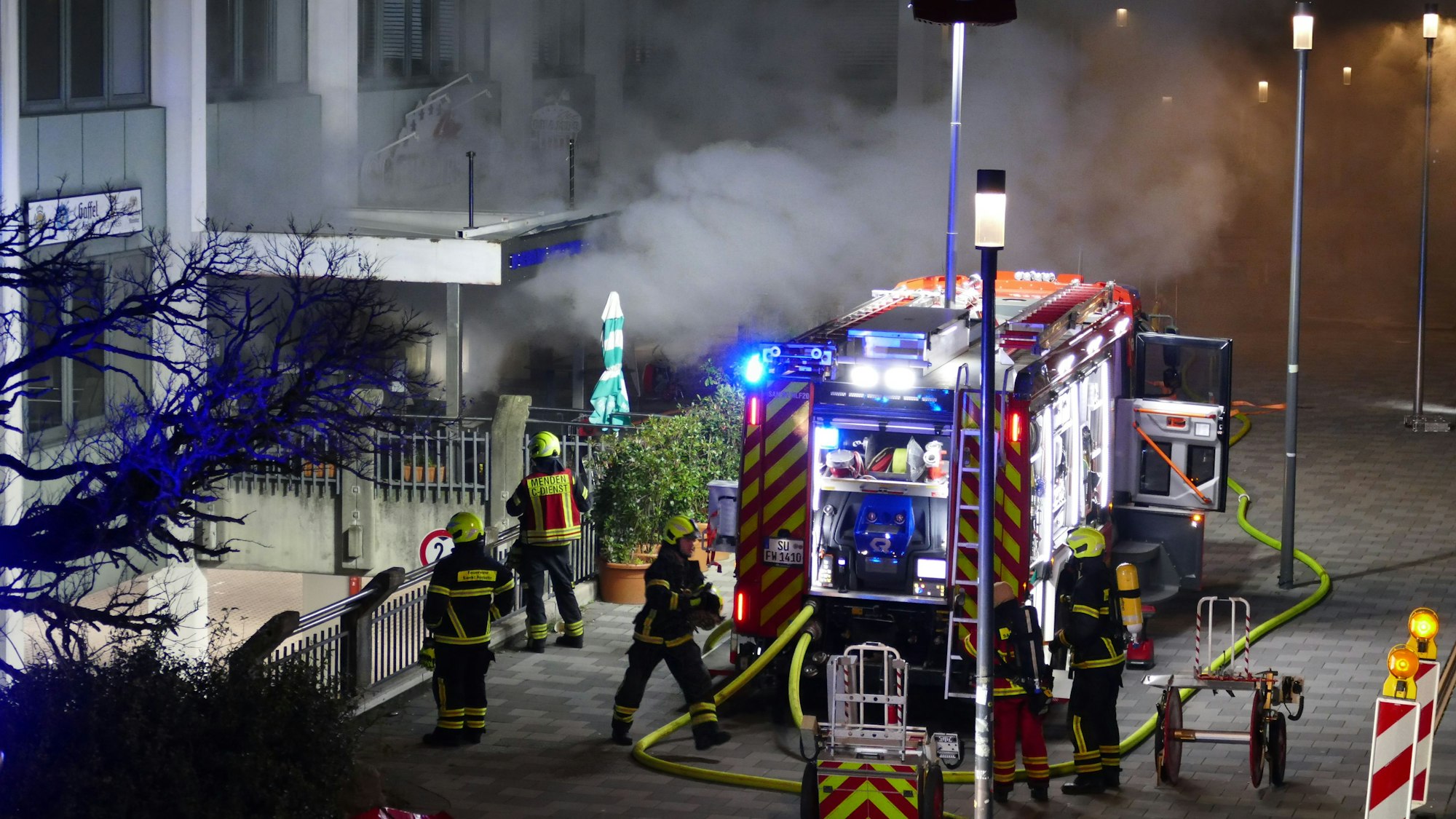 Rauch dringt aus einem Gebäude, ein Feuerwehrfahrzeug steht davor.