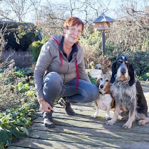 Franziska Weyer hockt in einem Garten neben zwei Hunden, einem Basset und einem Griffon.