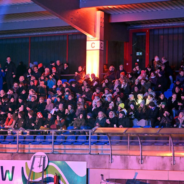 Menschen sitzen auf der illuminierten Tribüne des Bergisch Gladbacher Stadions und singen.