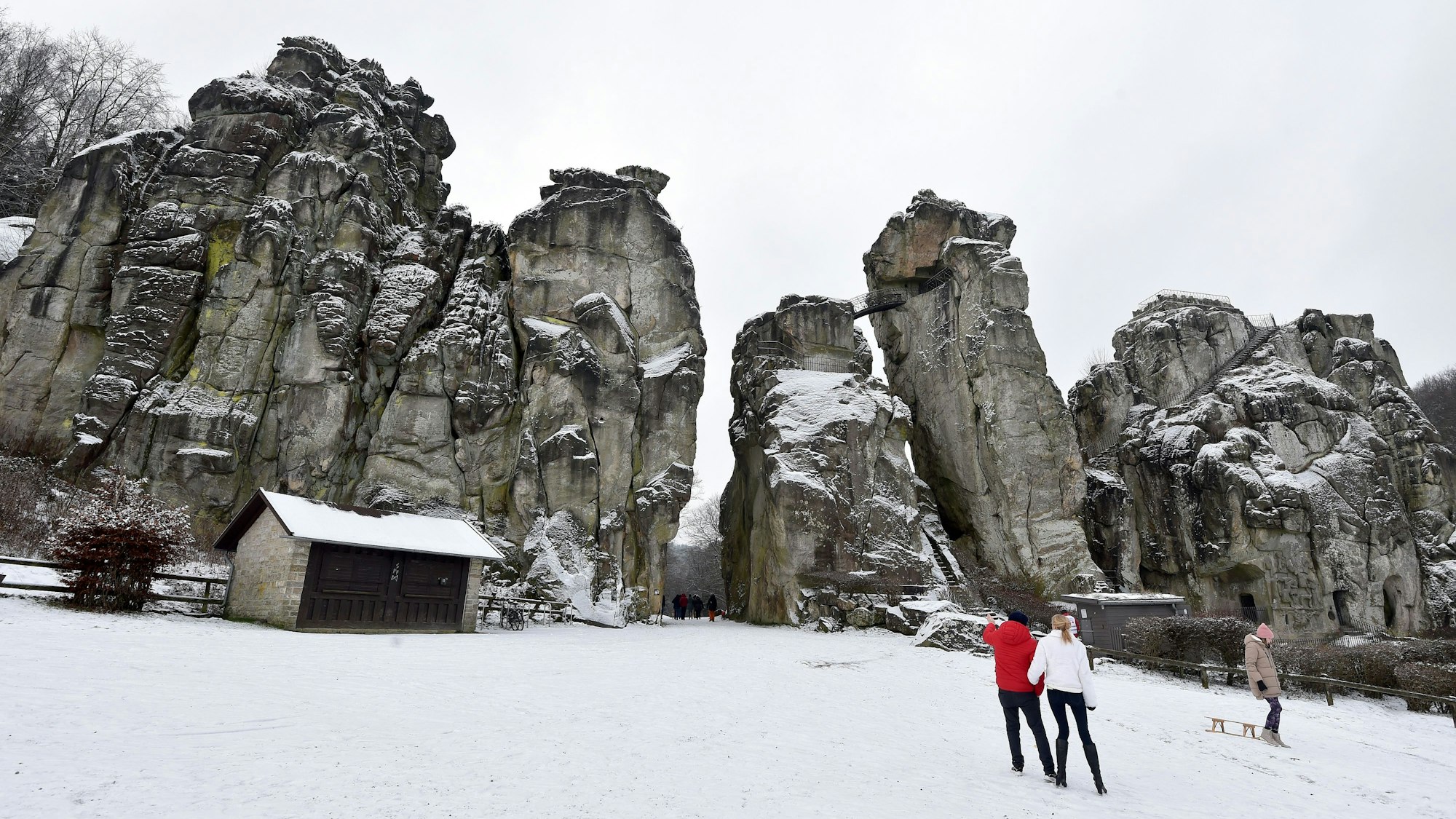 Spaziergänger stehen vor den schneebedeckten Externsteinen