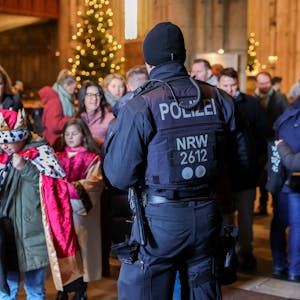 Zu sehen in ein Polizeibeamter vor verkleideten jungen Kindern. Es geht um die Aussendung der Sternsinger im Kölner Dom.