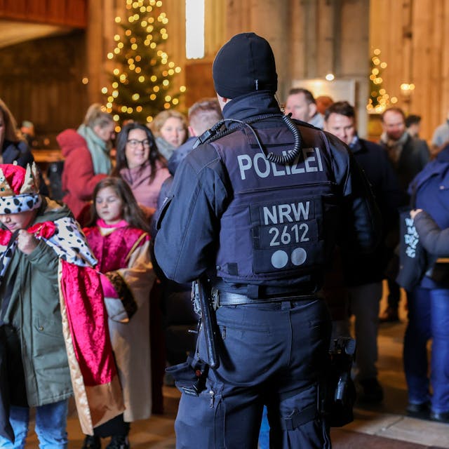 Zu sehen in ein Polizeibeamter vor verkleideten jungen Kindern. Es geht um die Aussendung der Sternsinger im Kölner Dom.