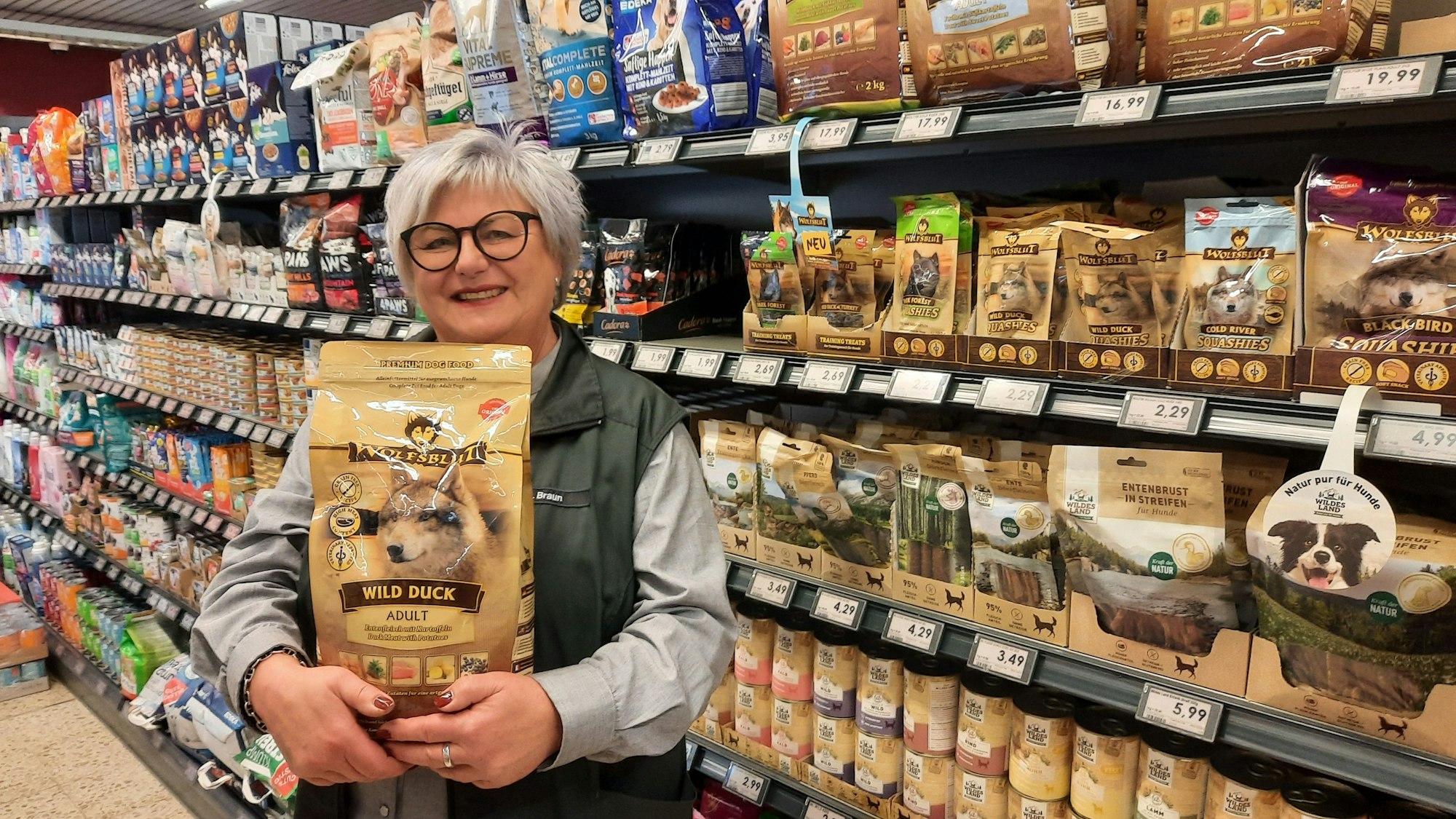 Birgit Braun steht in einem Supermarkt und hält eine Packung Hundefutter in den Händen.