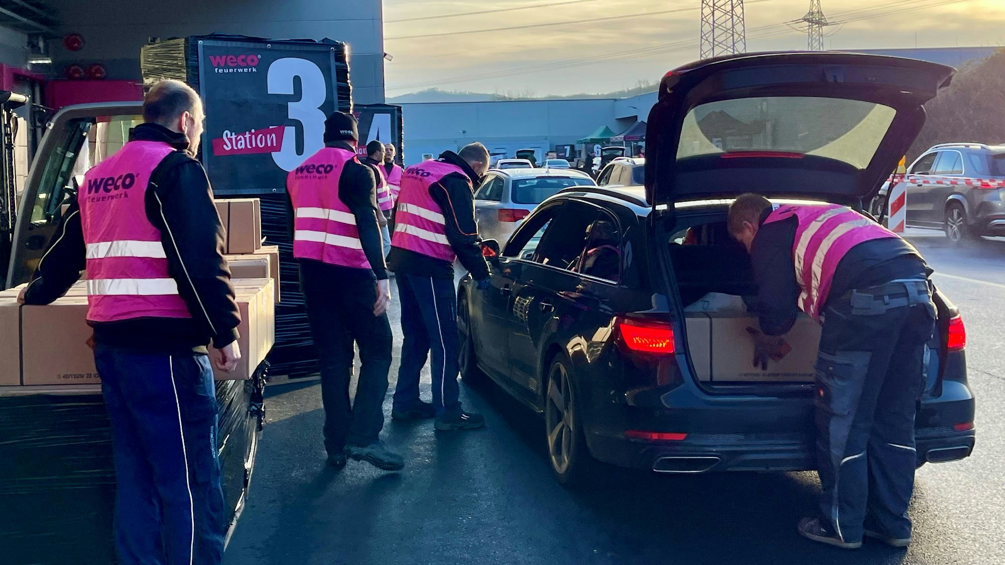 Männer in pinkfarbenen Weco-Westen beladen ein Auto mit langen Paketen.