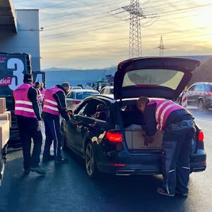 Männer in pinkfarbenen Weco-Westen beladen ein Auto mit langen Paketen.