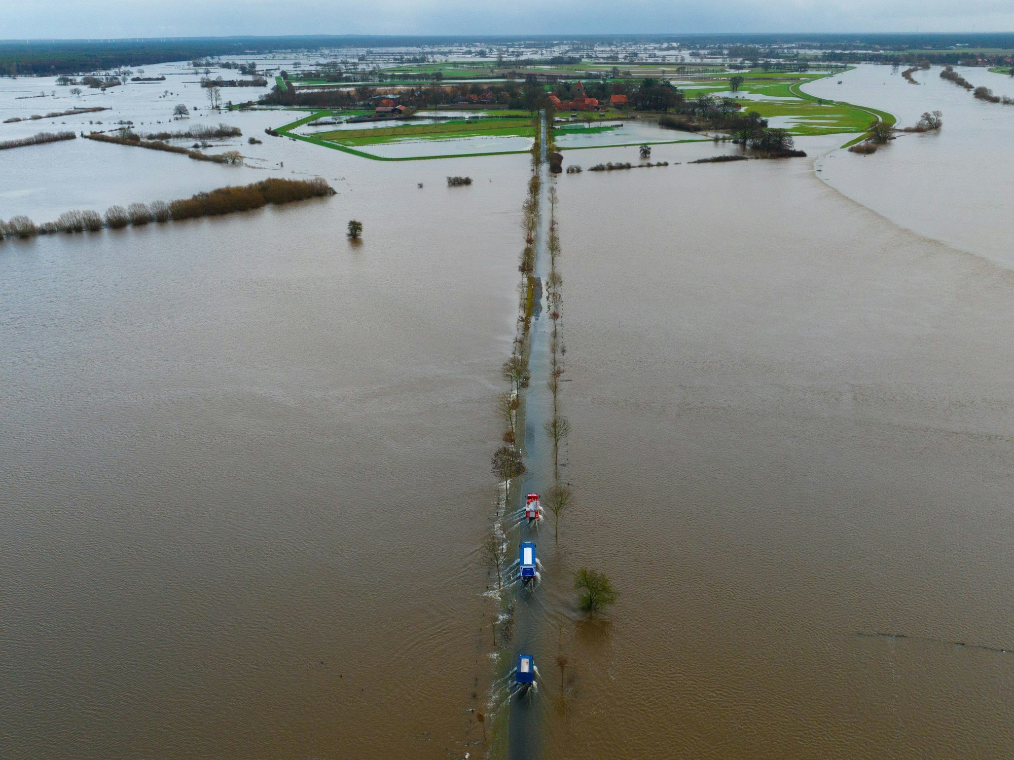Ein Fahrzeug vom THW sowie der Feuerwehr fahren auf einer teilweise überfluteten Straße unweit der Aller (Aufnahme mit einer Drohne), hier in Kirchwahlingen in Niedersachsen.
