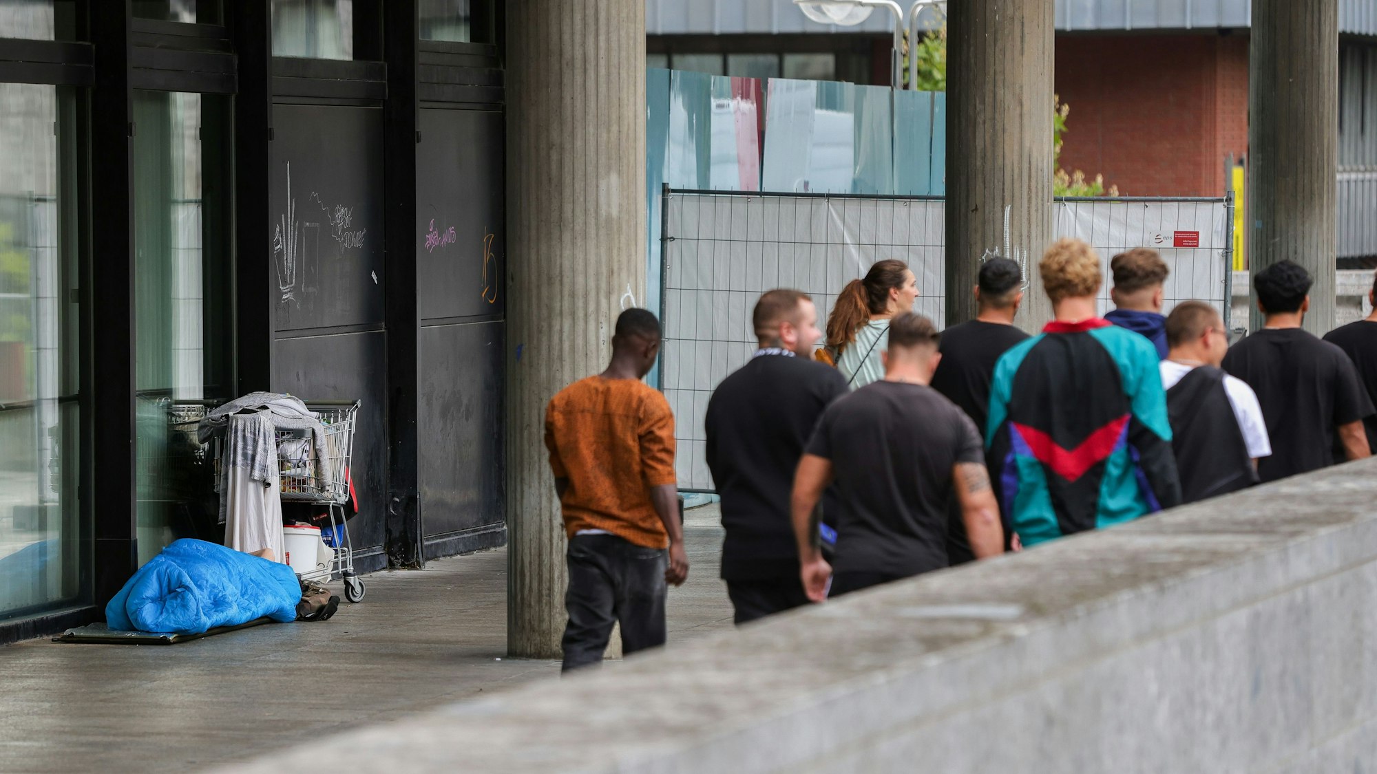 Ein wohl obdachloser Mensch liegt in der Nähe des Kölner Doms, daneben eine Gruppe junger Männer.
