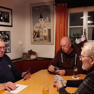 Drei Männer sitzen in einer Kneipe am Tisch und spielen Karten. An der Wand hängt ein Ölbild von E.O. Primbsch, das die Kaller Pfarrkirche zeigt.