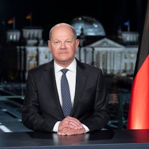 Bundeskanzler Olaf Scholz bei seiner Neujahrsansprache für 2024. Er sitzt an einem dunklen Tisch, neben ihm eine Deutschlandflagge und die Flagge der Europäischen Union.