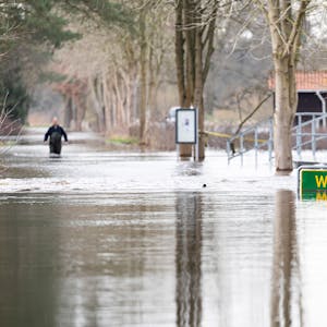 Eine Person läuft auf einer überfluteten Straße in der Siedlung Westohe der Gemeinde Winsen (Aller) im Landkreis Celle.