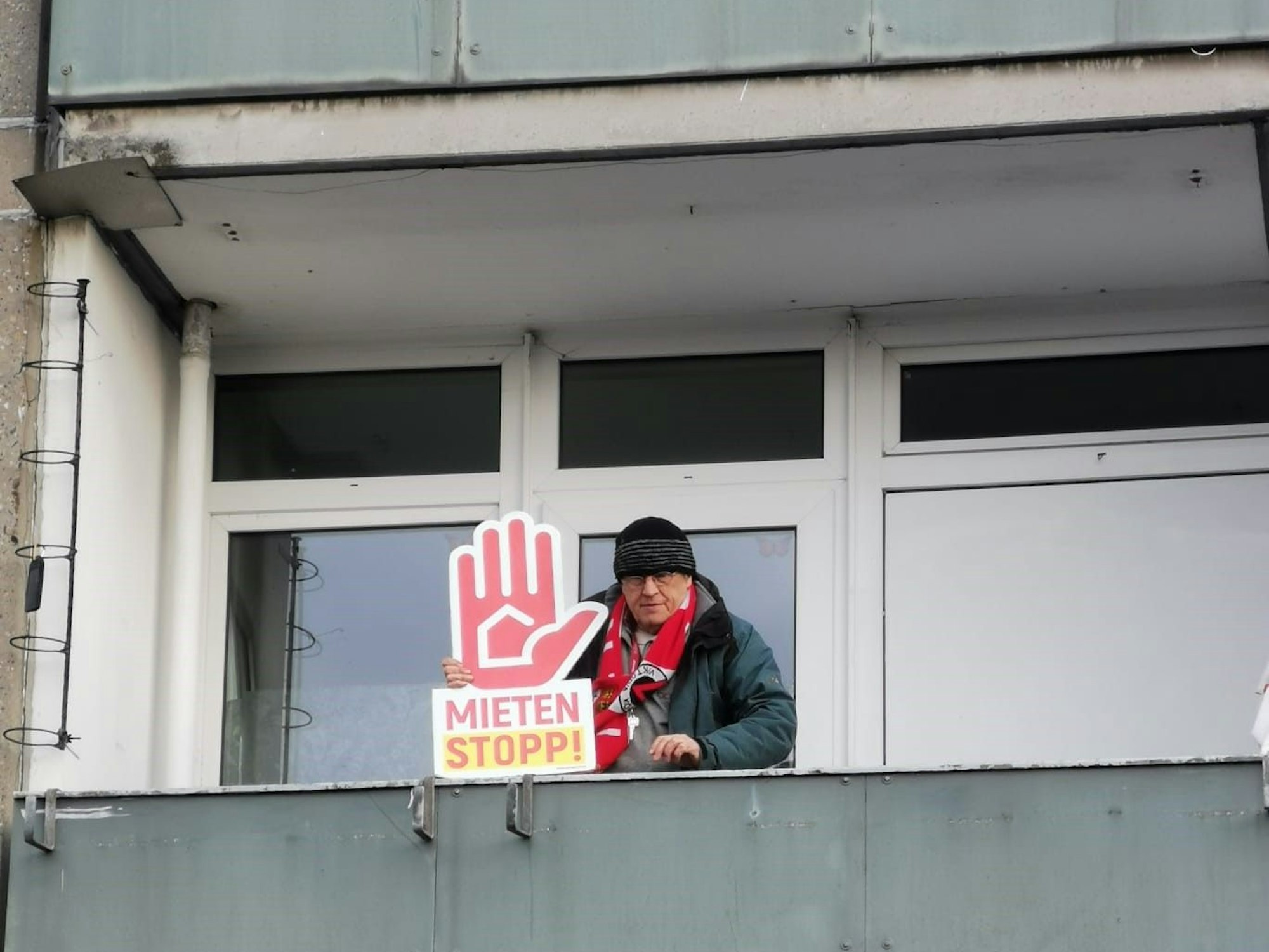 Rainer Kippe steht auf einem Balkon und hält ein Plakat mit der Forderung "Mieten Stopp" in der Hand.