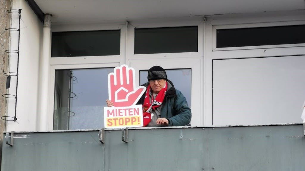 Rainer Kippe steht auf einem Balkon und hält ein Plakat mit der Forderung "Mieten Stopp" in der Hand.&nbsp;