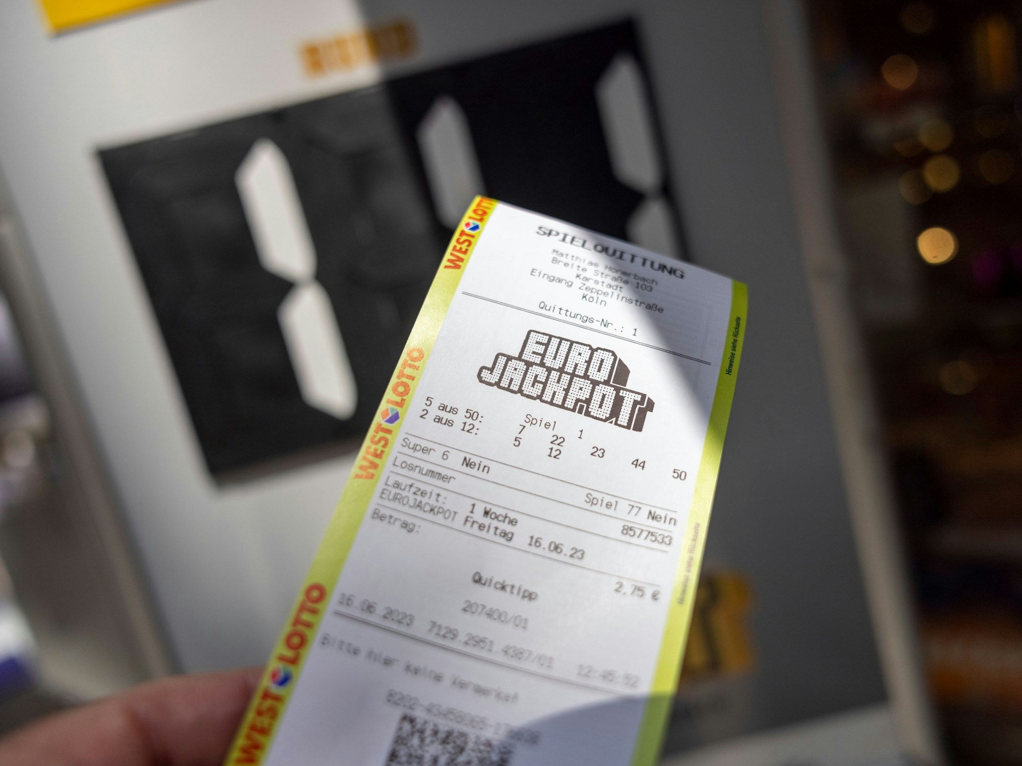 Eine Spielquittung für ein Eurojackpot-Los wird von einem Kunden in einer Lotto-Annahmestelle in die Kamera gehalten.