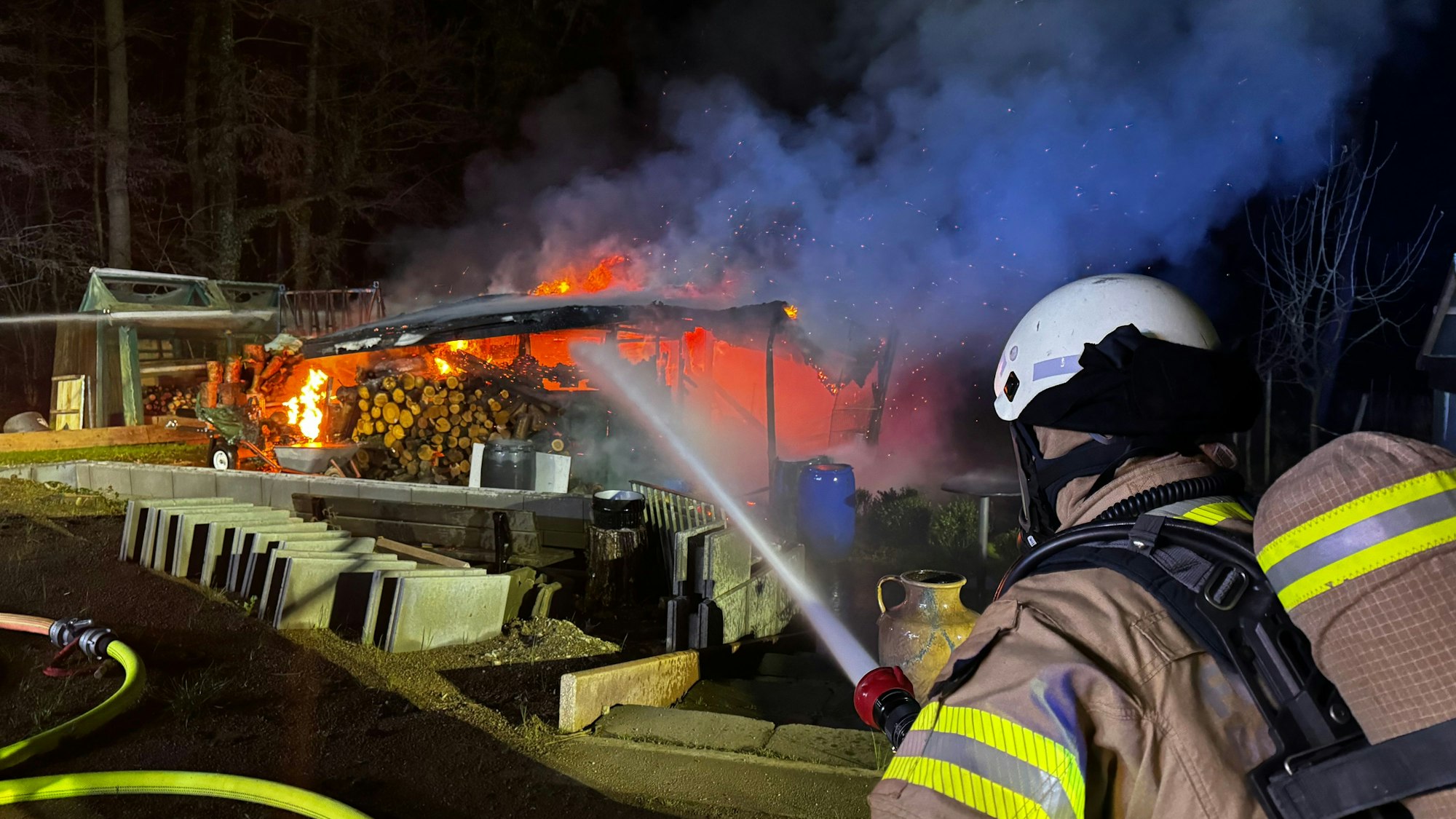 Ein Feuerwehrmann zielt mit einem Löschrohr auf einen brennenden Holzstapel.