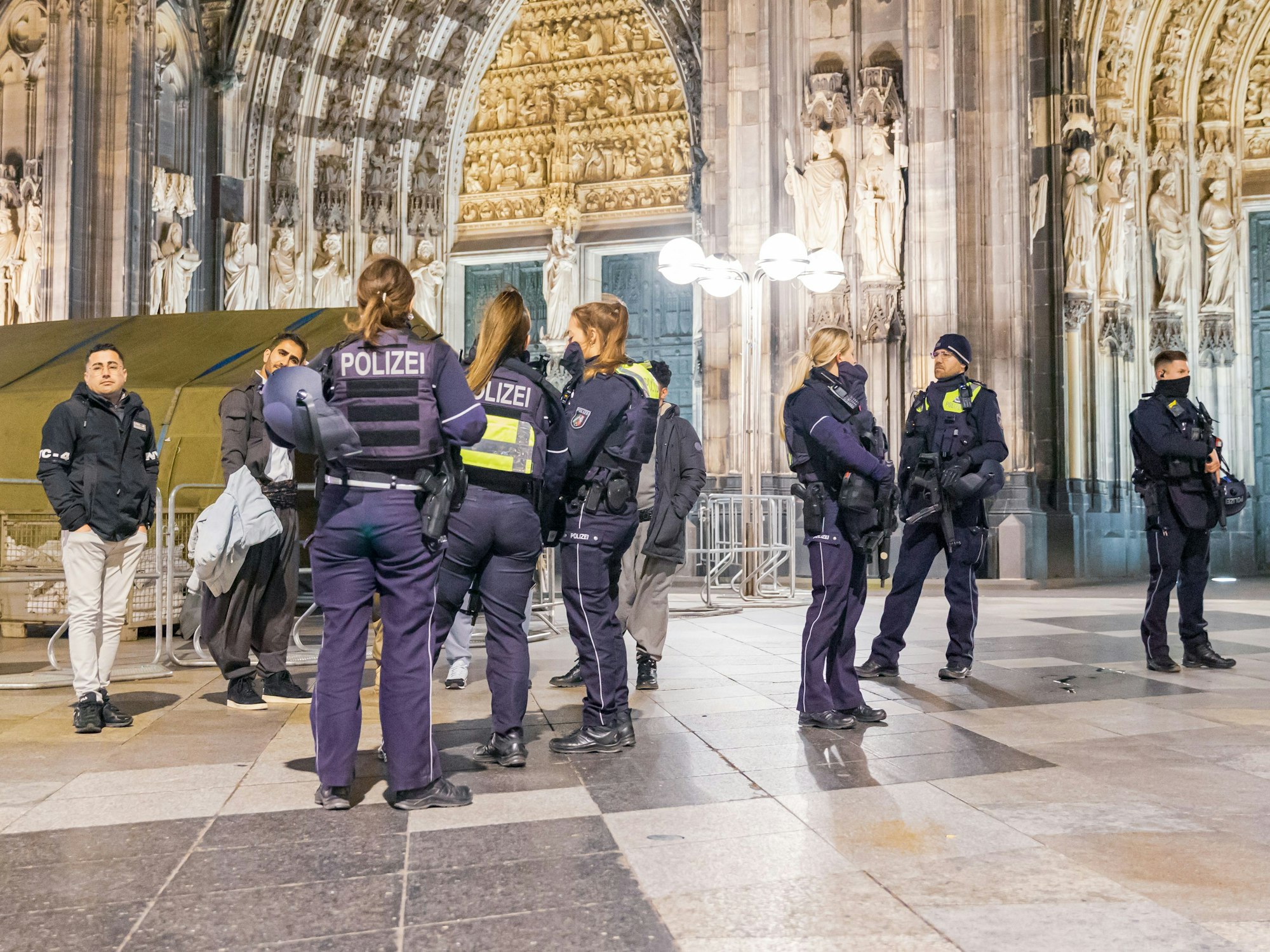 Einsatzkräfte der Polizei stehen vor dem Eingang zum Kölner Dom und kontrollieren Feiernde.