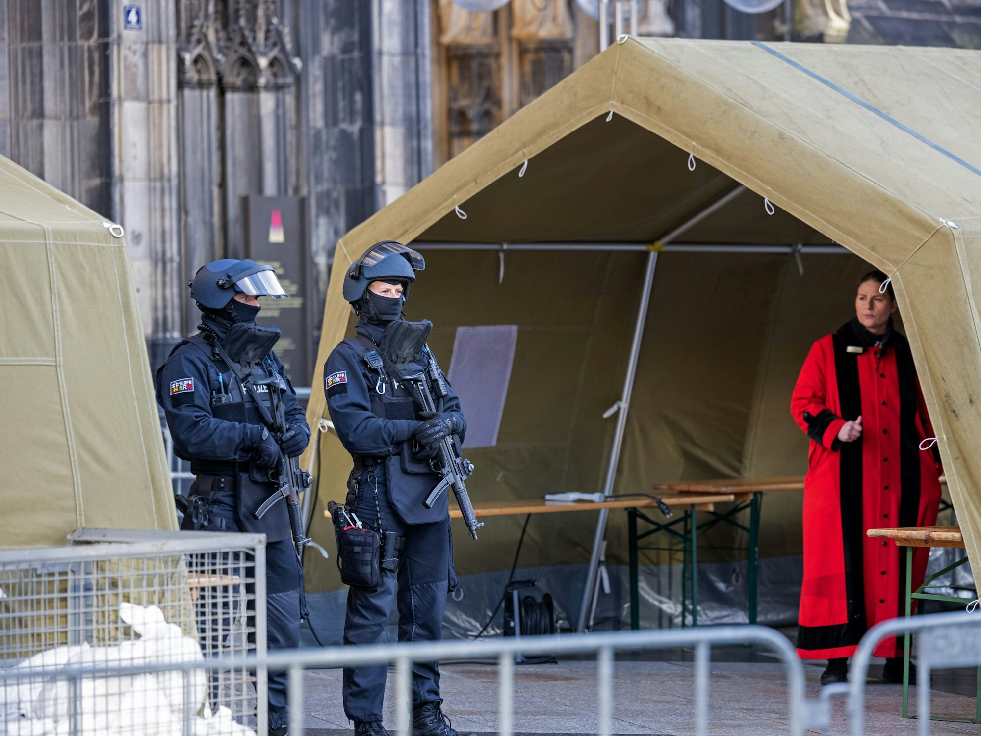 Zwei Polizisten mit Maschinenpistolen stehen zwischen Zelten vor dem Kölner Dom.