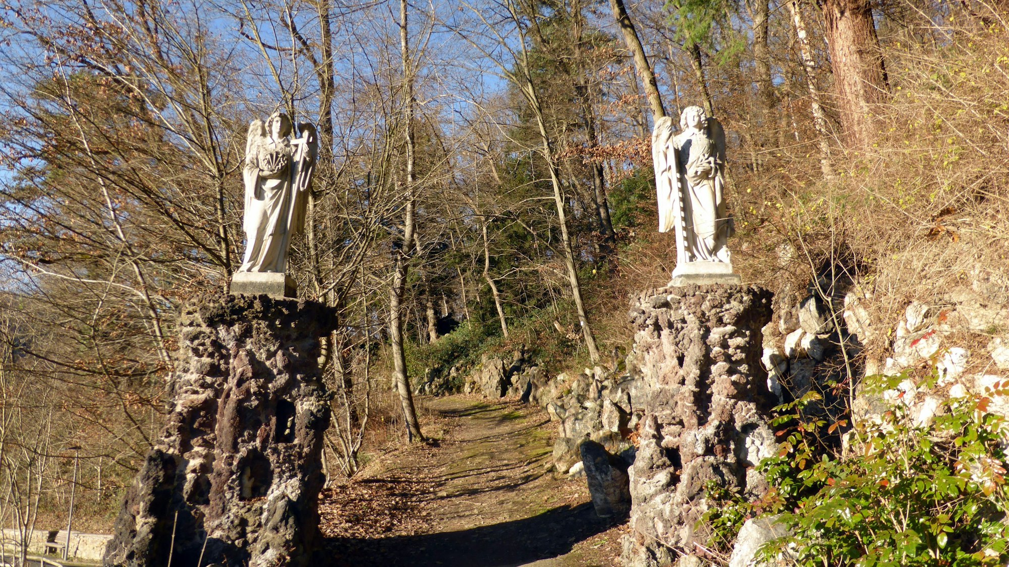 Zwei Engelsstatuen flankieren den Zugang zu einem Waldweg.