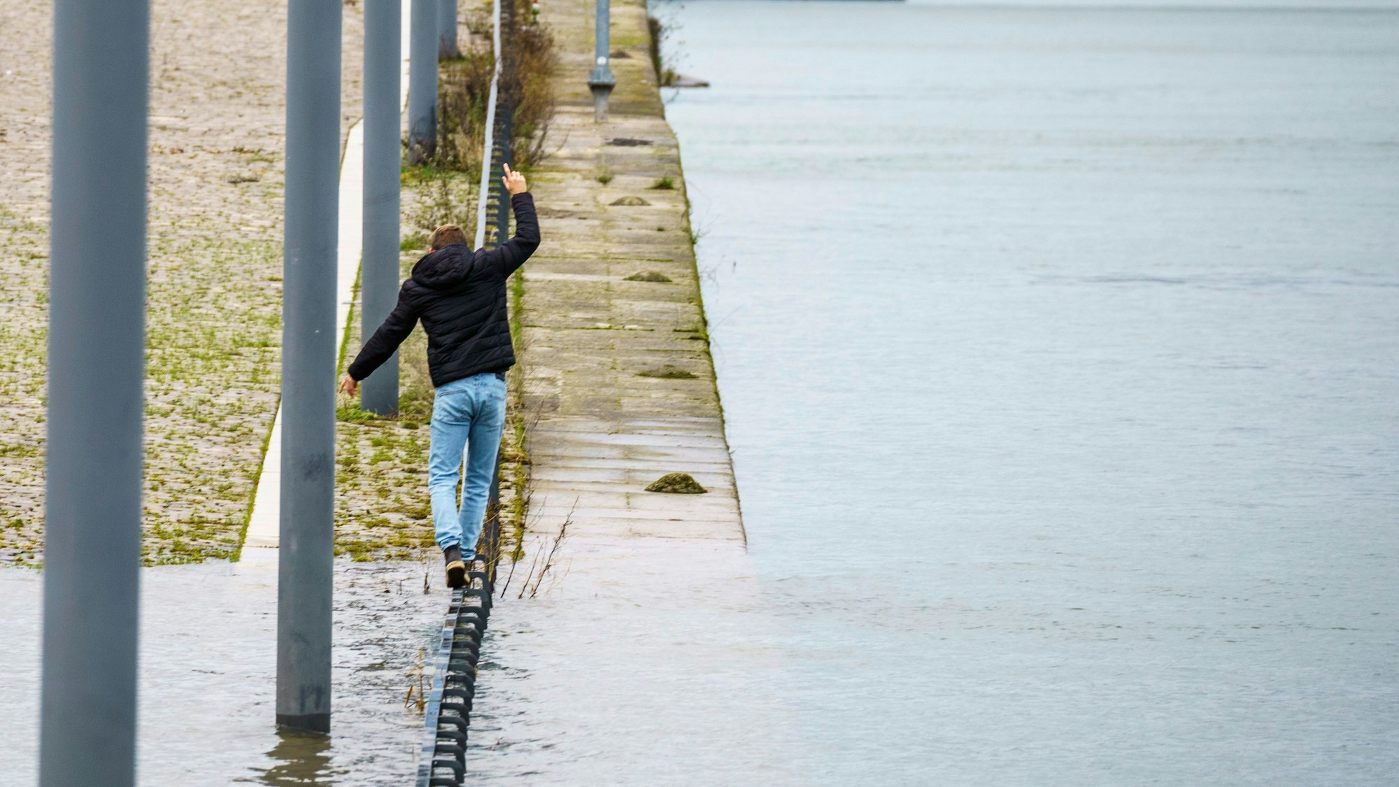 Ein Mann balanciert am Neujahrstag auf einem Geländer am Rheinufer, das leicht unter Wasser steht.