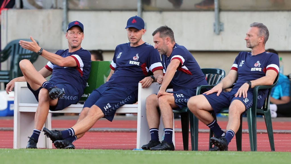 Die damaligen Baumgart-Assistenten Kevin McKenna, René Wagner, André Pawlak und Uwe Gospodarek sitzen beim FC-Testspiel in Bergisch Gladbach nebeneinander am Spielfeldrand.