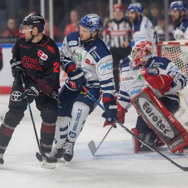 Zwei Eishockeyspieler stehen nah beieinander vor einem Tor mit einem weiteren Spieler.